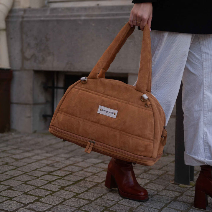 Sac à langer doudoune camel Baby on Board porté à la main, un modèle sophistiqué et pratique pour les parents en déplacement.