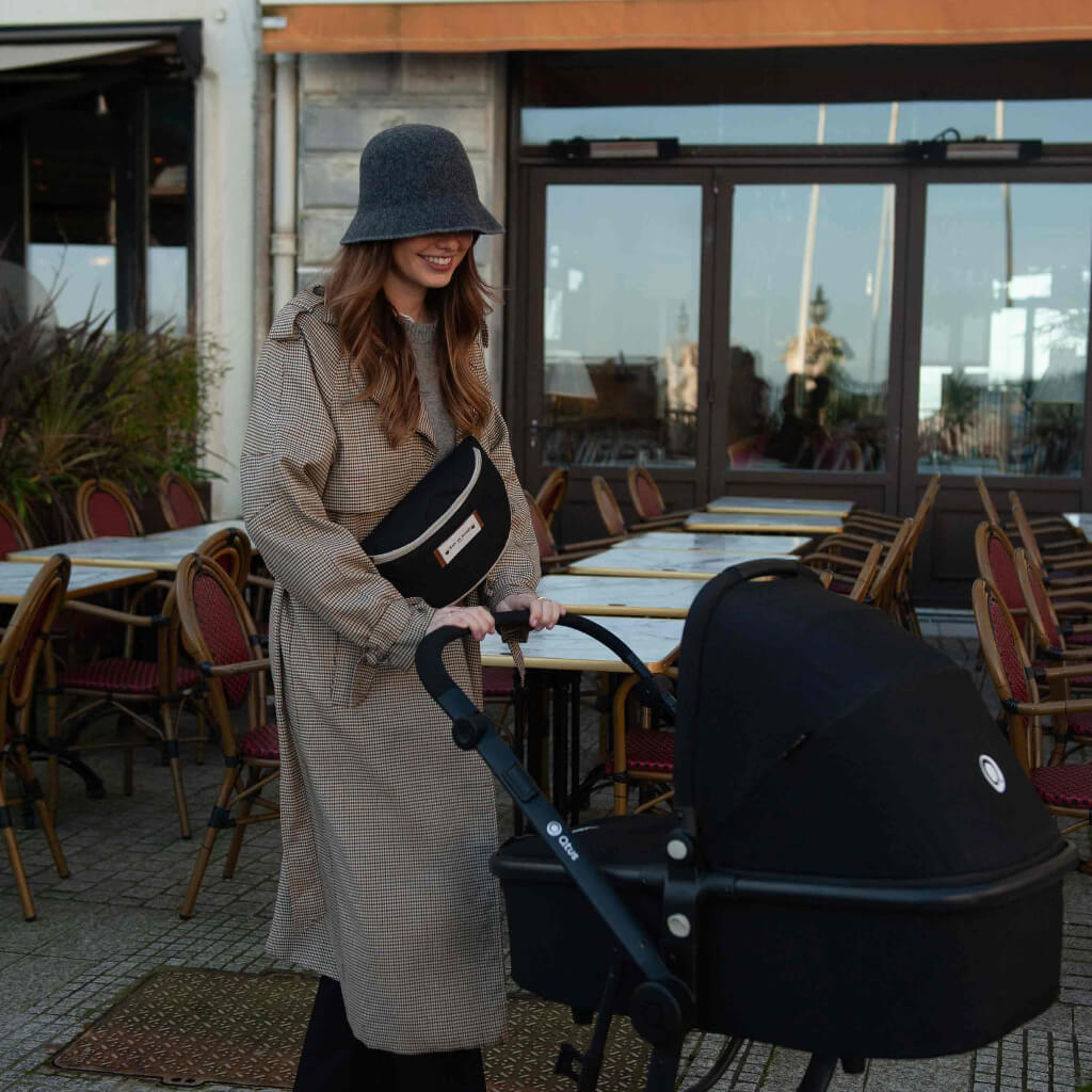 Jeune maman en balade avec une poussette, portant le sac banane à langer Armelle noir Baby on Board en bandoulière, chic et pratique.